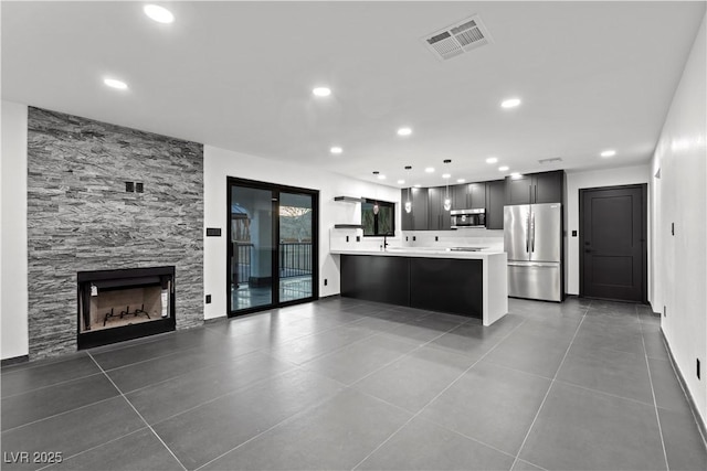 kitchen with a fireplace, tile patterned floors, kitchen peninsula, hanging light fixtures, and appliances with stainless steel finishes