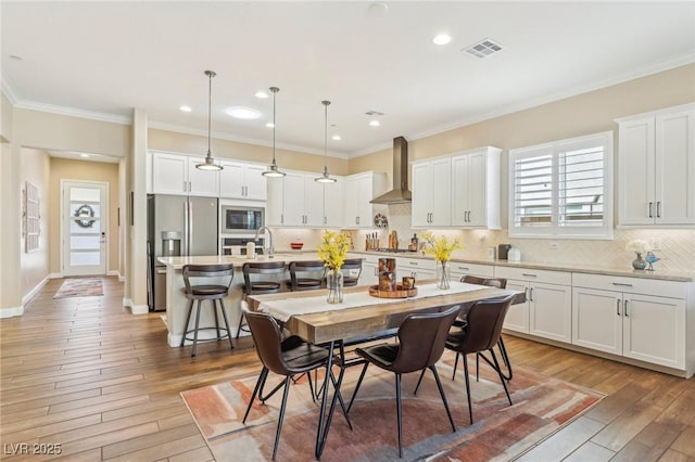 kitchen with white cabinetry, wall chimney range hood, stainless steel appliances, and hanging light fixtures