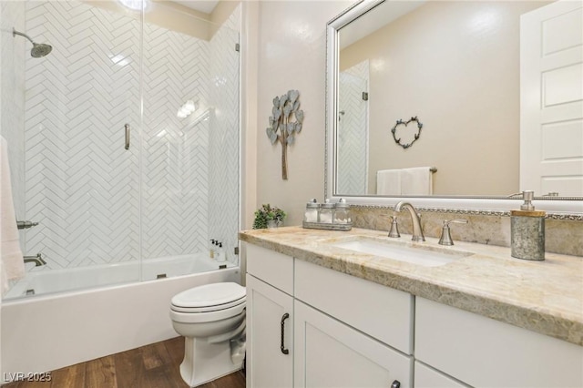 full bathroom with hardwood / wood-style flooring, tiled shower / bath combo, vanity, and toilet