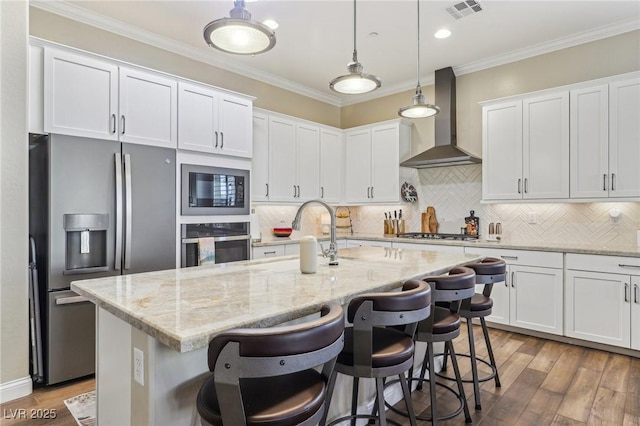 kitchen featuring stainless steel appliances, wall chimney exhaust hood, and a center island with sink