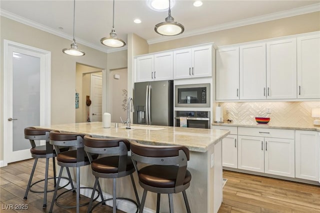 kitchen featuring decorative light fixtures, a center island with sink, decorative backsplash, appliances with stainless steel finishes, and white cabinets