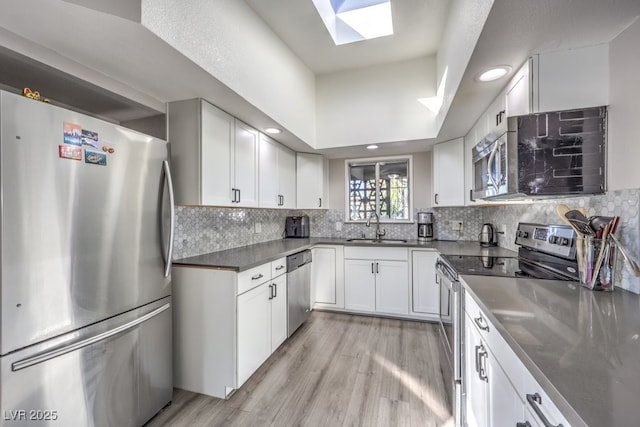 kitchen featuring white cabinets, appliances with stainless steel finishes, a skylight, sink, and light hardwood / wood-style flooring