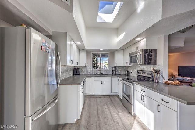 kitchen featuring sink, backsplash, a skylight, stainless steel appliances, and white cabinets