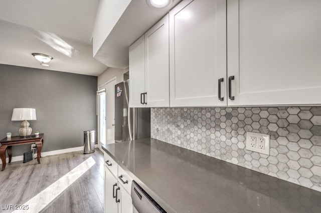 kitchen with white cabinetry, backsplash, stainless steel dishwasher, and light hardwood / wood-style flooring