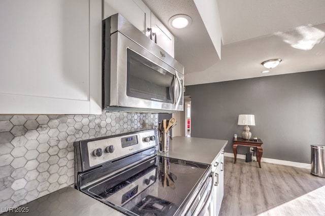 kitchen featuring white cabinets, appliances with stainless steel finishes, backsplash, and light hardwood / wood-style flooring