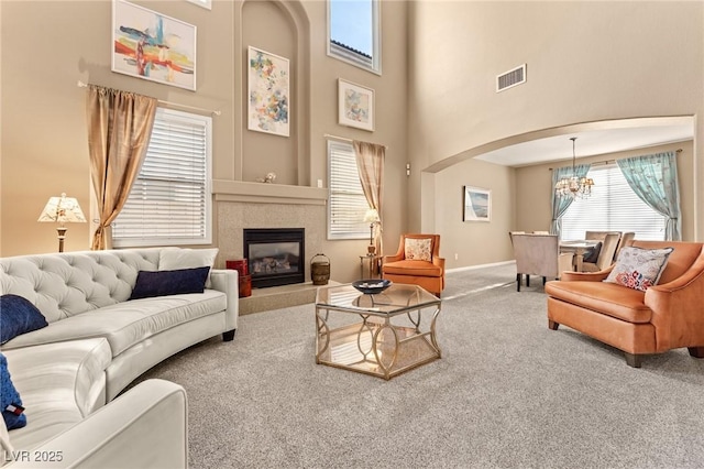 carpeted living room featuring a high ceiling, a tile fireplace, and a notable chandelier