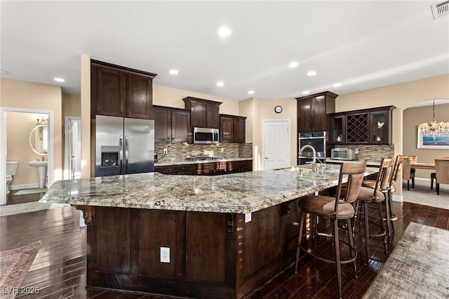 kitchen with a spacious island, stainless steel appliances, dark brown cabinets, and backsplash