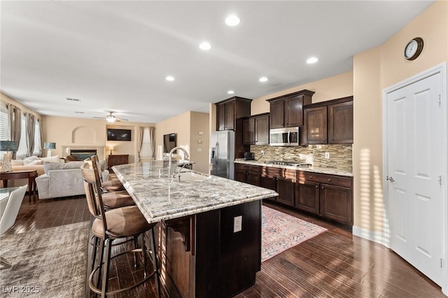 kitchen featuring sink, appliances with stainless steel finishes, a kitchen bar, backsplash, and a center island with sink