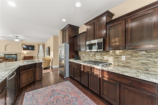 kitchen featuring dark wood-type flooring, dark brown cabinetry, light stone counters, tasteful backsplash, and appliances with stainless steel finishes