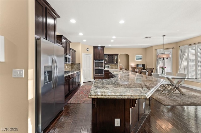 kitchen with dark wood-type flooring, tasteful backsplash, pendant lighting, stainless steel appliances, and a large island