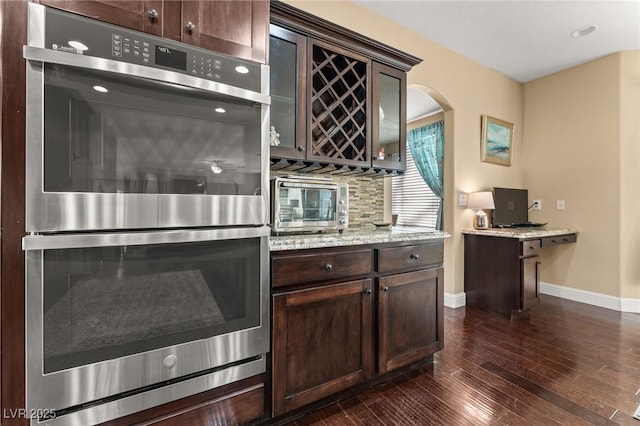 kitchen with dark hardwood / wood-style flooring, light stone countertops, double oven, and dark brown cabinets