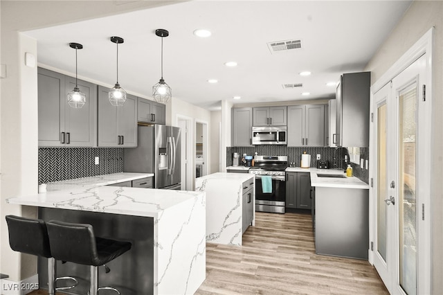 kitchen with kitchen peninsula, a kitchen bar, hanging light fixtures, gray cabinetry, and stainless steel appliances