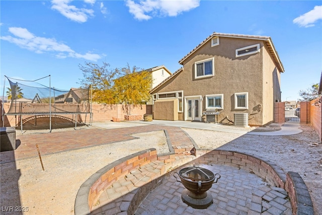 rear view of house with central air condition unit, a trampoline, a patio area, a fire pit, and french doors