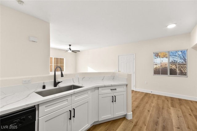 kitchen featuring light stone counters, sink, white cabinets, and black dishwasher