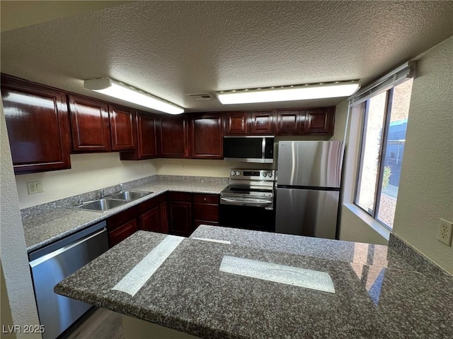 kitchen featuring sink, kitchen peninsula, a textured ceiling, and appliances with stainless steel finishes