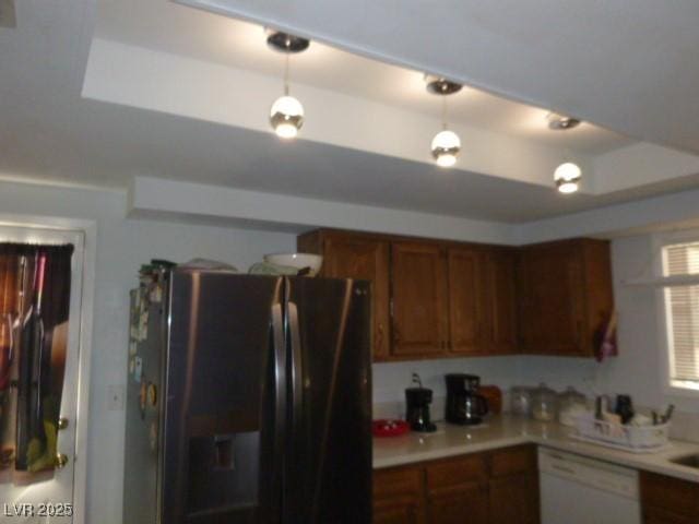 kitchen featuring a tray ceiling, stainless steel fridge, decorative light fixtures, and white dishwasher