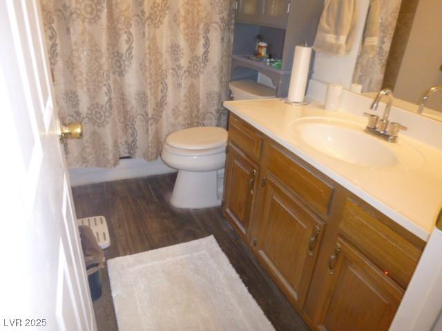 full bathroom with hardwood / wood-style flooring, shower / tub combo with curtain, vanity, and toilet