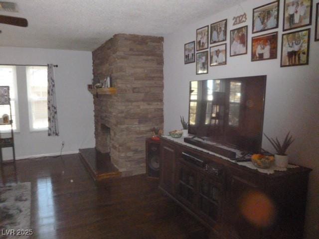 living room with dark hardwood / wood-style flooring, ceiling fan, a stone fireplace, and a textured ceiling