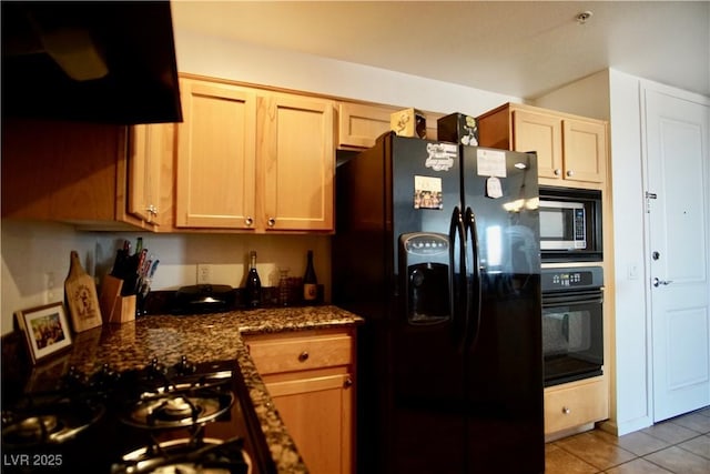 kitchen with light brown cabinetry, ventilation hood, dark stone countertops, light tile patterned floors, and black appliances