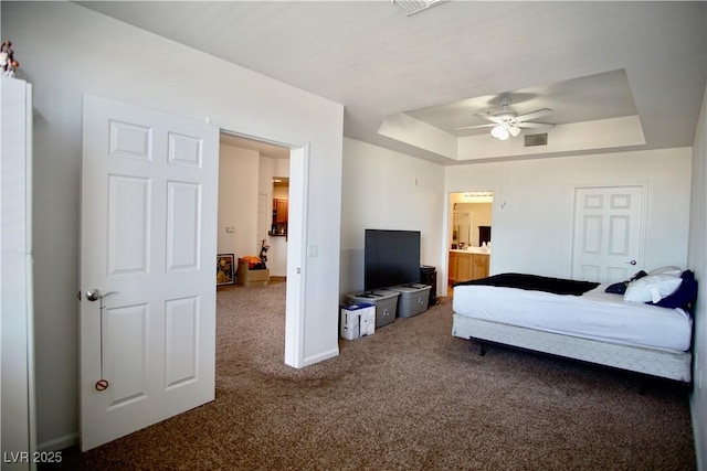 bedroom featuring ceiling fan, connected bathroom, a tray ceiling, and dark carpet