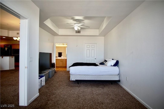 bedroom featuring dark carpet, a tray ceiling, ceiling fan, and ensuite bathroom