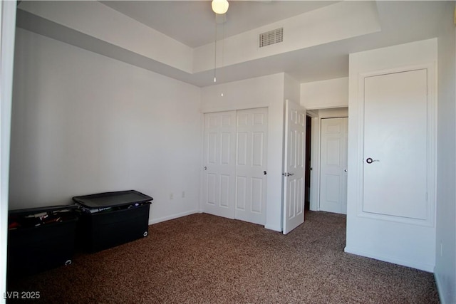 unfurnished bedroom featuring a tray ceiling, a closet, and dark colored carpet