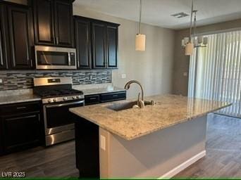 kitchen featuring hanging light fixtures, appliances with stainless steel finishes, tasteful backsplash, and an island with sink