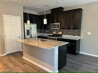 kitchen with appliances with stainless steel finishes, backsplash, a kitchen island with sink, dark hardwood / wood-style flooring, and sink