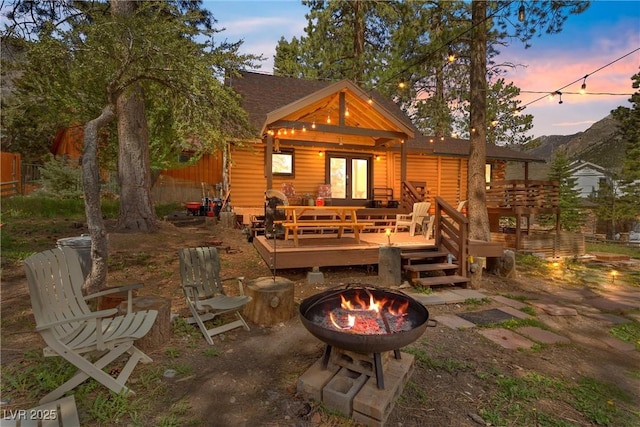 back house at dusk featuring a deck and a fire pit