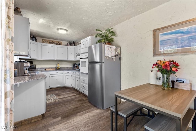 kitchen featuring dark hardwood / wood-style flooring, oven, a textured ceiling, white cabinets, and stainless steel refrigerator