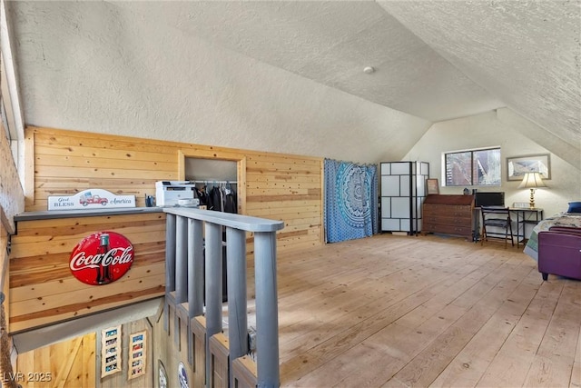 additional living space with vaulted ceiling, hardwood / wood-style flooring, a textured ceiling, and wood walls