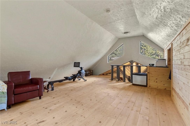 bonus room featuring vaulted ceiling, wood walls, a textured ceiling, and hardwood / wood-style floors