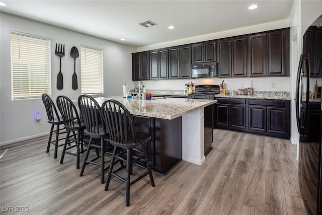 kitchen with black appliances, light hardwood / wood-style floors, sink, a kitchen island with sink, and a breakfast bar