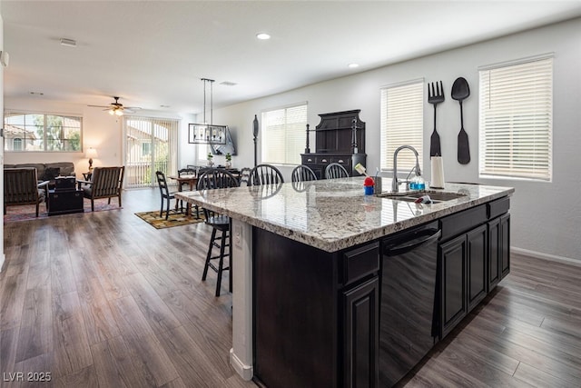 kitchen with a breakfast bar, sink, black dishwasher, hanging light fixtures, and a kitchen island with sink