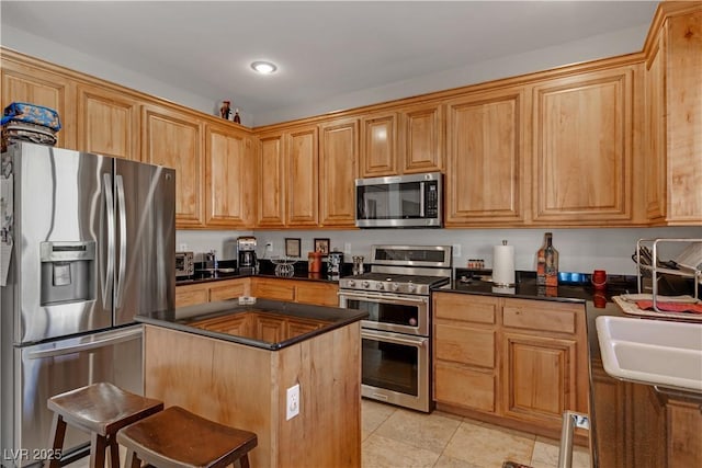 kitchen with light tile patterned flooring, appliances with stainless steel finishes, a breakfast bar, sink, and a center island