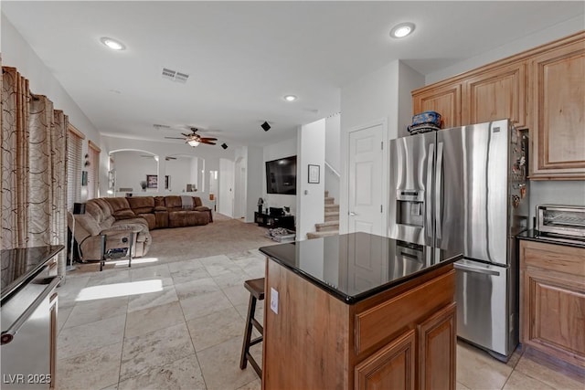 kitchen with ceiling fan, a breakfast bar, stainless steel fridge, and a center island