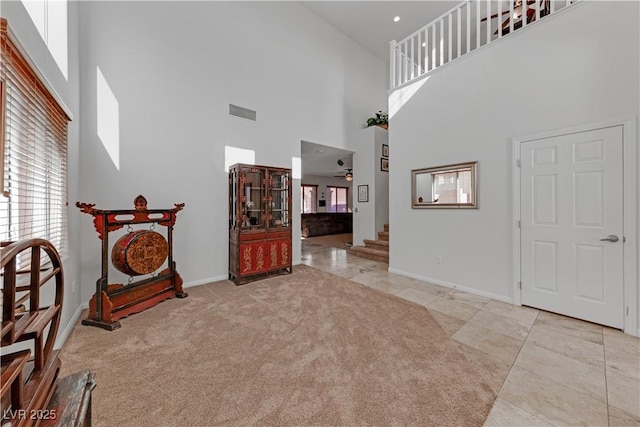 entrance foyer with ceiling fan, light colored carpet, and a towering ceiling