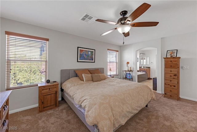 bedroom featuring ceiling fan, light colored carpet, connected bathroom, and multiple windows