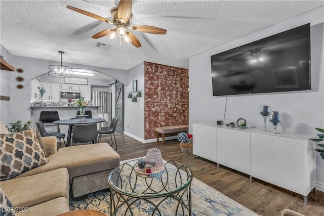 living room featuring ceiling fan with notable chandelier, a textured ceiling, and dark hardwood / wood-style floors