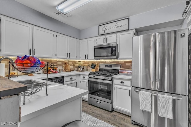 kitchen with hardwood / wood-style floors, white cabinetry, sink, backsplash, and stainless steel appliances