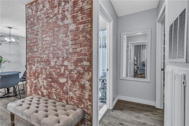 corridor featuring light hardwood / wood-style floors, a textured ceiling, brick wall, and a notable chandelier