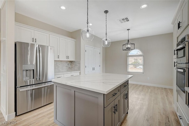 kitchen featuring a center island, hanging light fixtures, light stone countertops, stainless steel appliances, and white cabinets