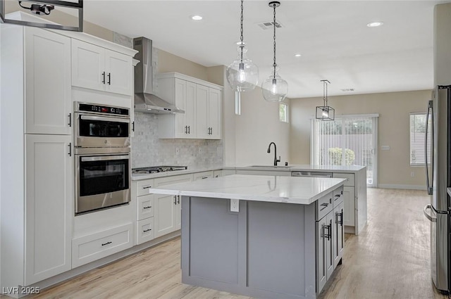 kitchen with a center island, kitchen peninsula, sink, stainless steel appliances, and wall chimney exhaust hood