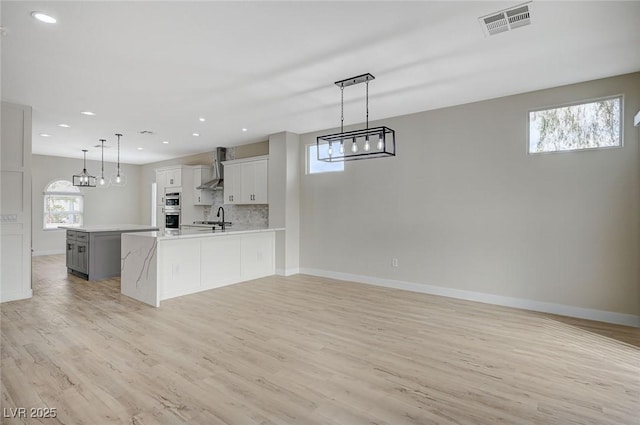 kitchen with backsplash, pendant lighting, sink, white cabinetry, and wall chimney exhaust hood