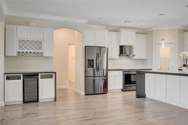 kitchen with appliances with stainless steel finishes, white cabinetry, wall chimney range hood, wine cooler, and light hardwood / wood-style floors