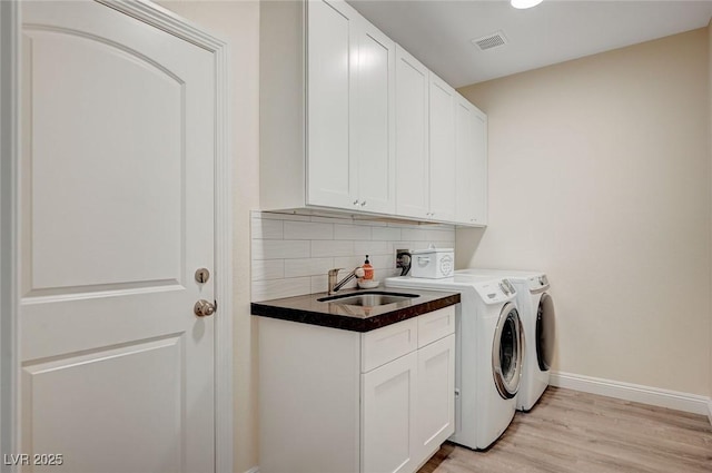 clothes washing area featuring light wood-type flooring, cabinets, washing machine and clothes dryer, and sink