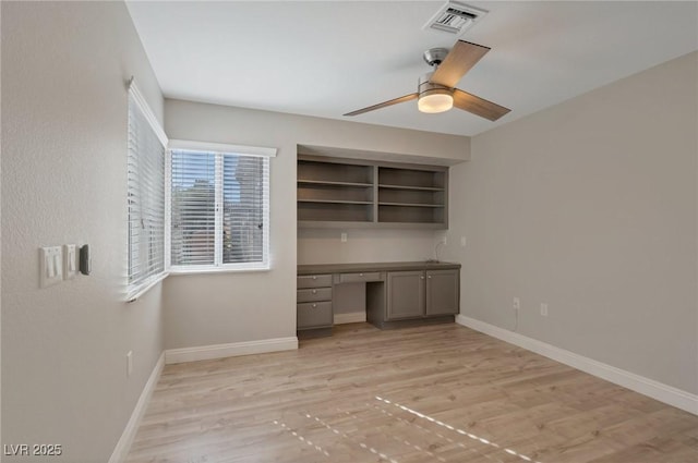 unfurnished office with built in desk, ceiling fan, and light wood-type flooring