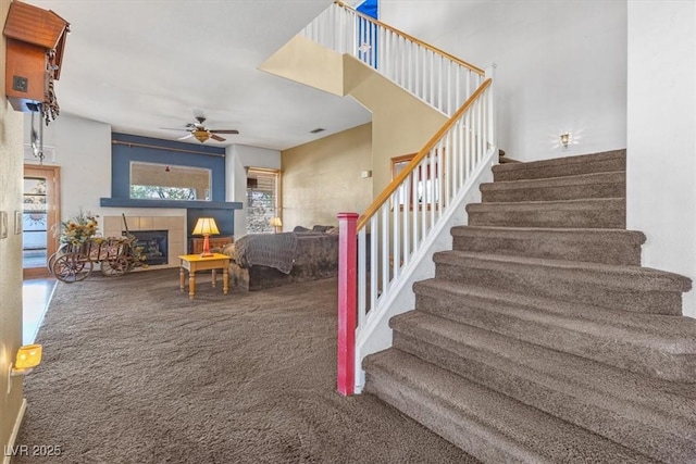 stairway with ceiling fan, carpet flooring, and a tiled fireplace