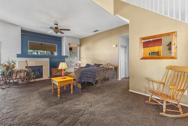 living room with carpet floors, ceiling fan, and a tiled fireplace