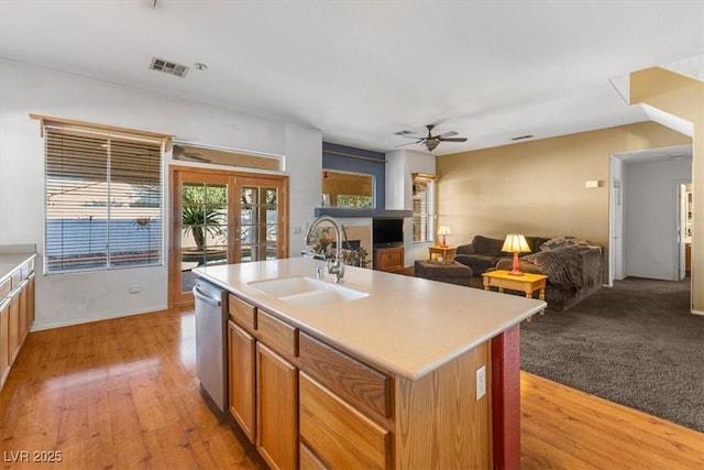 kitchen with french doors, light hardwood / wood-style floors, sink, stainless steel dishwasher, and a center island with sink